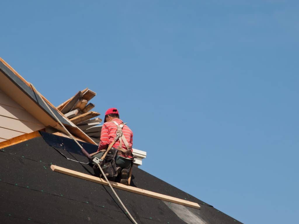 Construction worker installing roof shingles safely.
